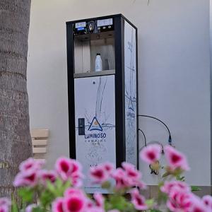 Water dispenser among pink flowers, evokes freshness and tranquility.