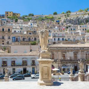Vue de Modica avec statues et maisons historiques.