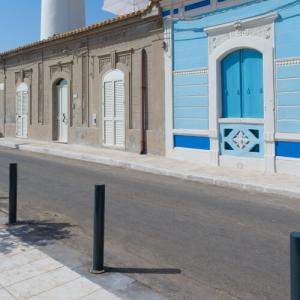 Rue avec maisons colorées et poteaux noirs, ciel clair.