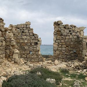 Ruines en pierre avec vue sur la mer sous un ciel nuageux.