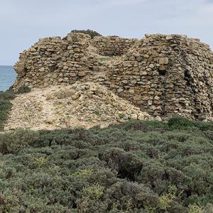 Ruines anciennes près de la mer, entourées de végétation.